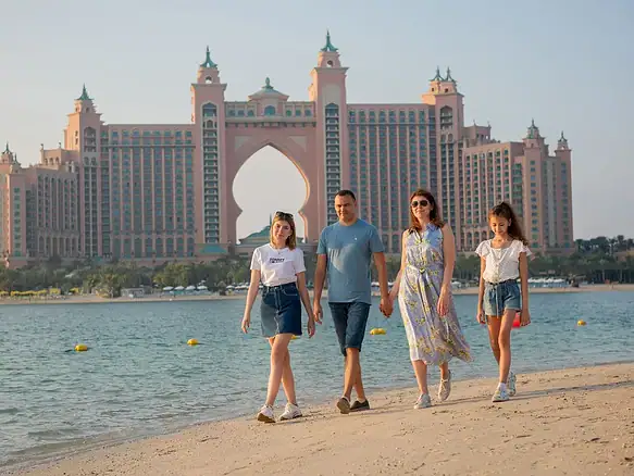 Rodina s dětmi na procházce po pláži na Palm Jumeirah v Dubaji, v pozadí hotel Atlantis