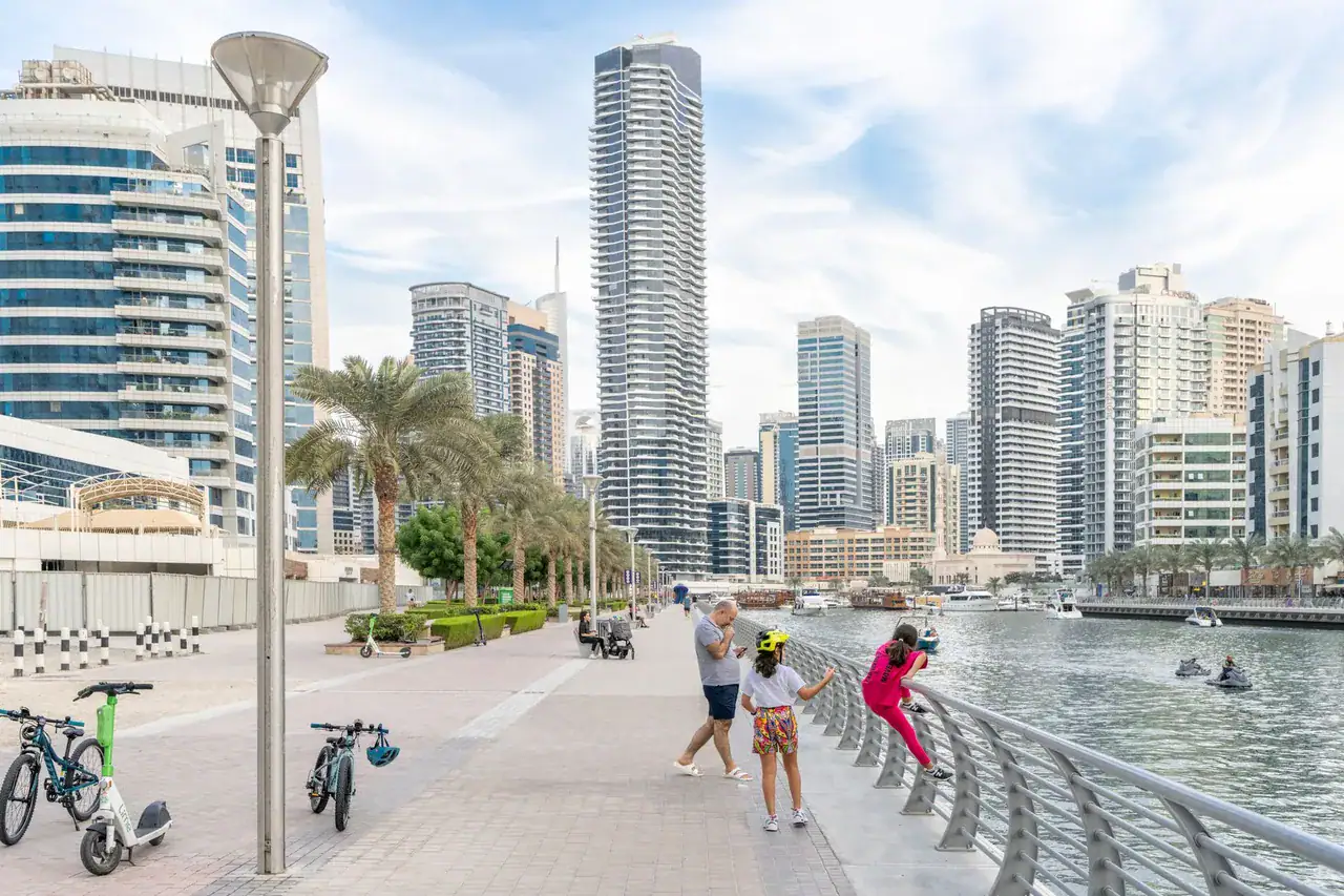 Tatínek s dcerami na promenádě Marina Walk v Dubai Marina, v pozadí obytné věže