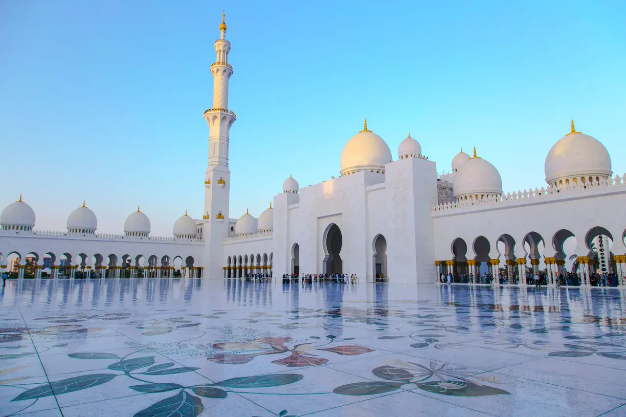 Nádvoří Sheikh Zayed Grand Mosque v Abú Dhabí s mramorovou mozaikou, bílými kupolemi a minaretem